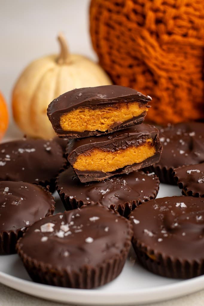 Chocolate pumpkin butter cups on a plate, two stacked and cut open to show the orange filling