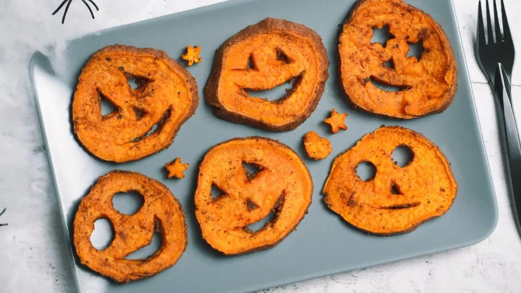 Roasted sweet potato rounds cut with jack-o’-lantern faces on a light blue plate
