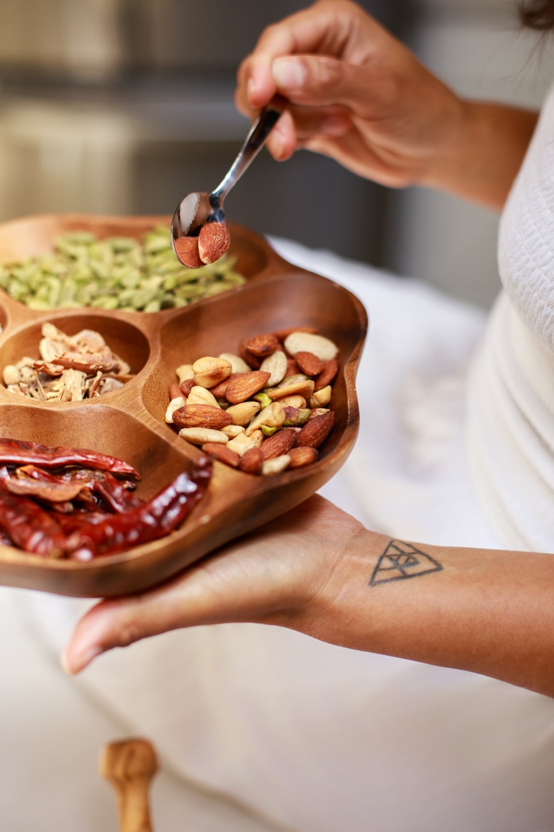 Hands holding a wooden tray of spices, nuts, and dried chilies