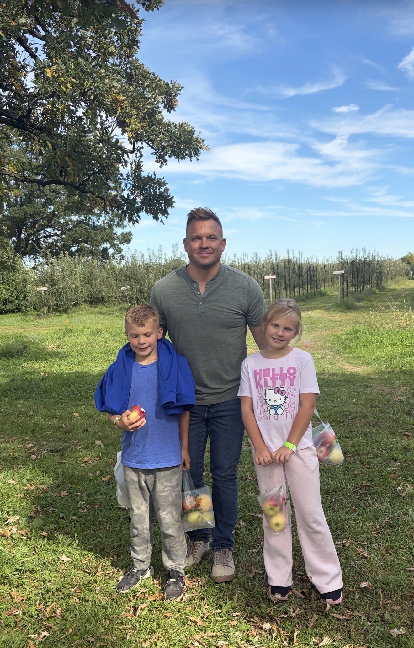 Jeremy Fojut with two children in an apple orchard, holding bags of apples