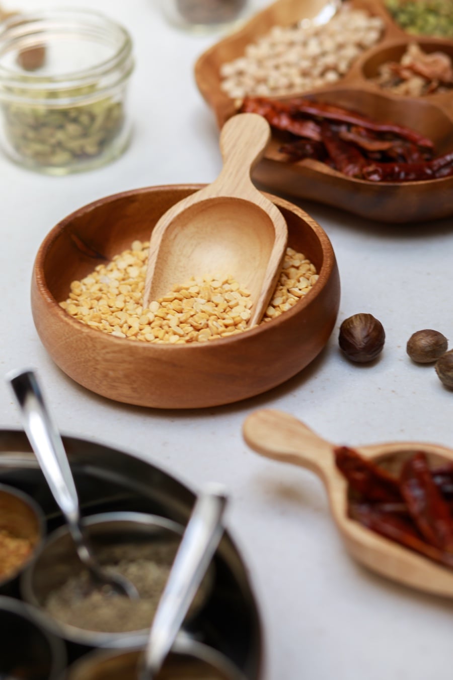 A wooden bowl of lentils with a scoop, surrounded by spices