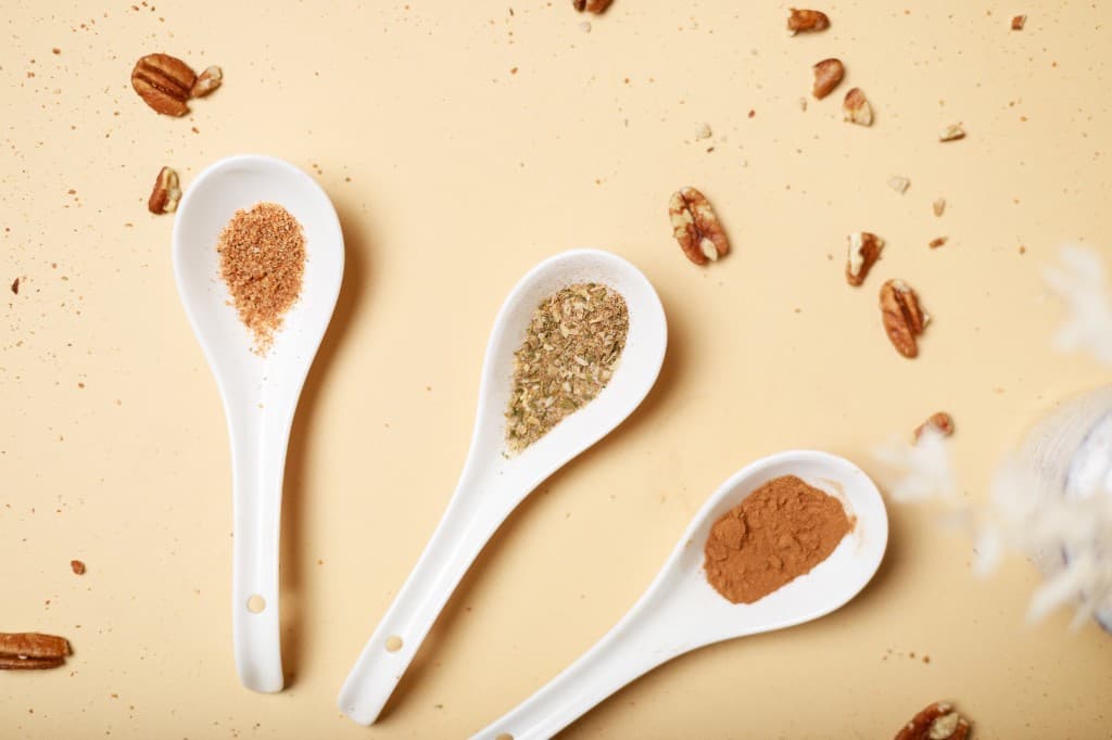 Three white spoons holding spices, with pecans scattered on a warm background